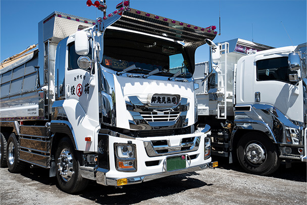 白とシルバーを基調としたダンプトラックが斜め前から撮影され、迫力のあるフロントデザインが目を引く。