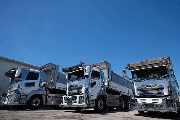 3台の大型ダンプトラックが整然と並び、青空の下で輝いている様子。