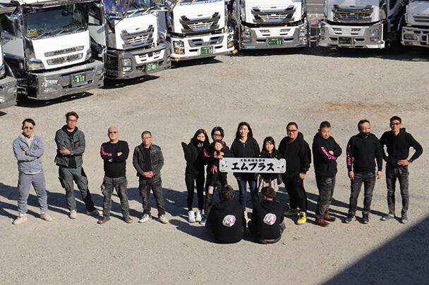 ダンプ車両の前に集合した株式会社エムプラスのスタッフ集合写真