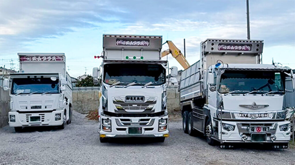 エムプラス所有の大型ダンプ3台が並ぶ駐車場風景