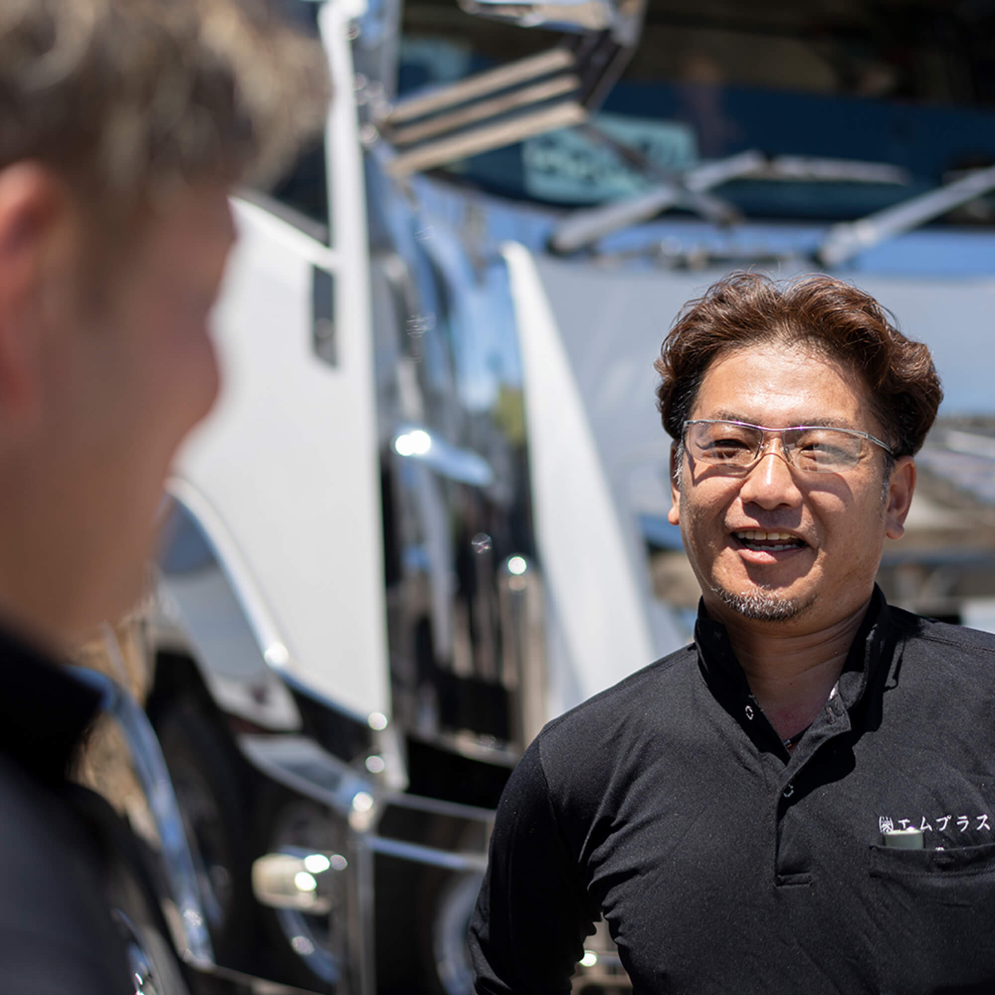 エムプラスのスタッフがトラックの前で笑顔で会話している様子。