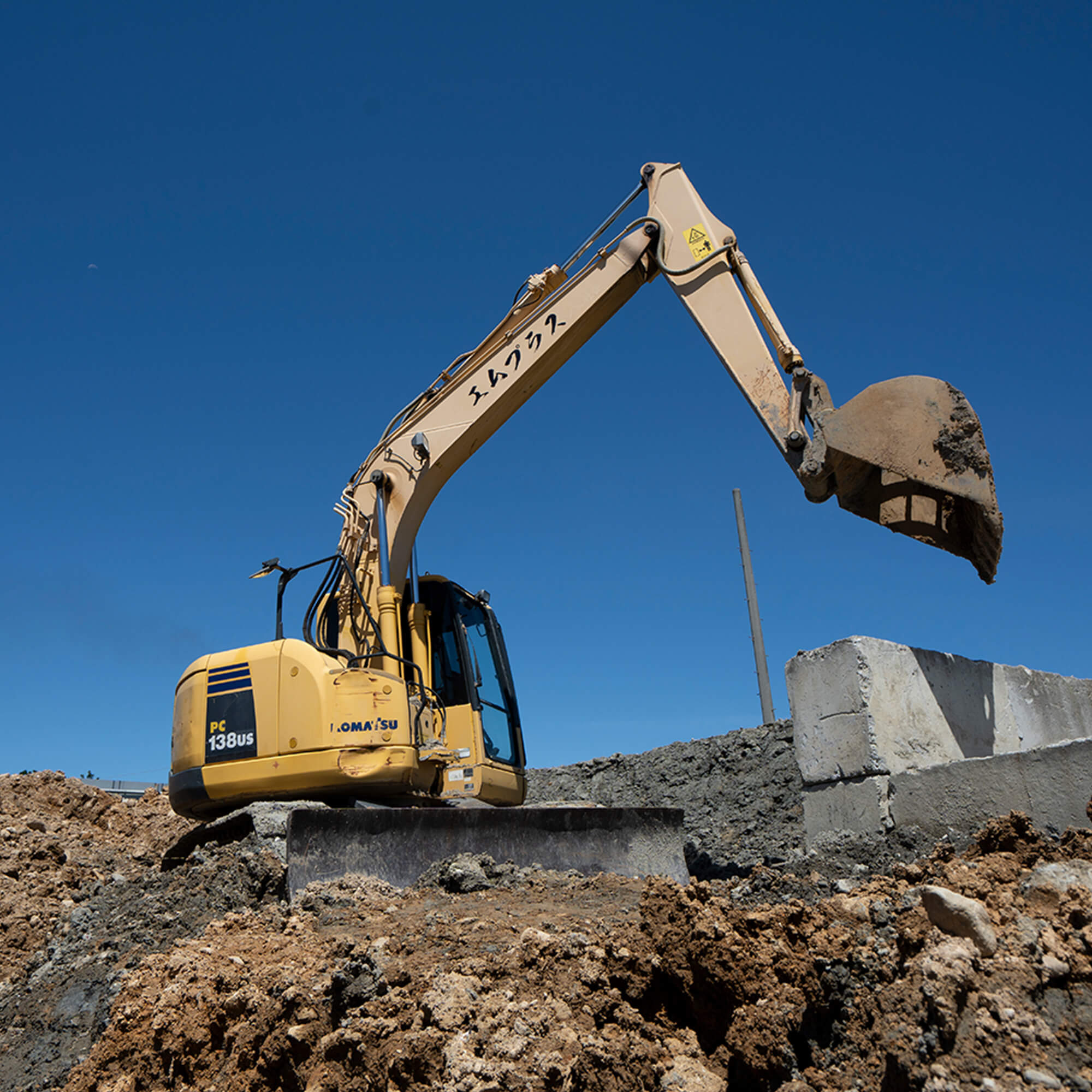 エムプラスと書かれたショベルカーが土をすくい上げている様子