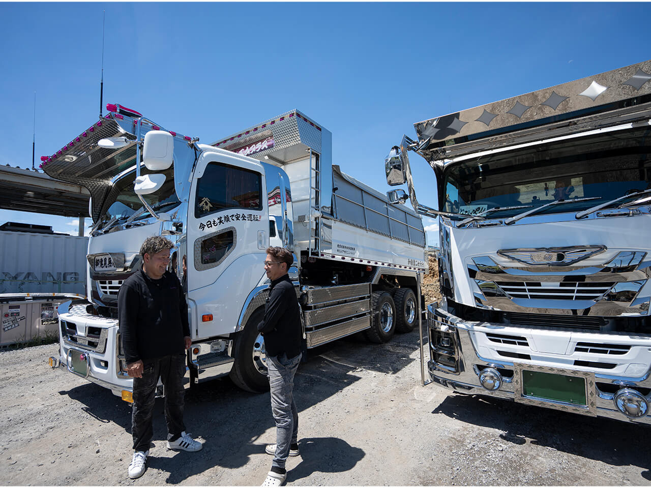 白い大型ダンプトラックの前で会話する作業着姿の男性二人