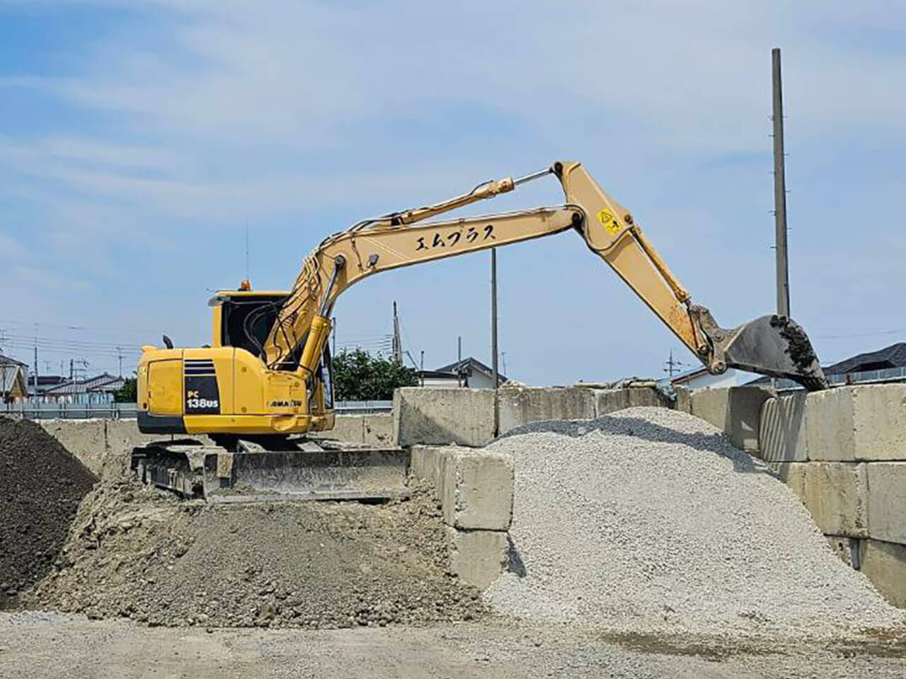空の下、建設残土の搬入・整地作業を行うエムプラスのユンボ